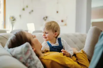 Kleinkind liegt auf dem Bauch seiner Mutter und schaut sie an.