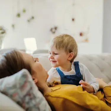 Kleinkind liegt auf dem Bauch seiner Mutter und schaut sie an.