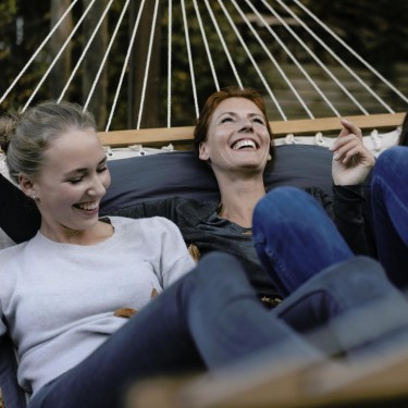 Gefühlsachterbahn Pubertät: Frau und zwei Teenagerinnen liegen lachend in einer Hängematte.