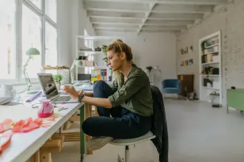 Multitasking: Frau sitzt an einem Schreibtisch am Laptop.