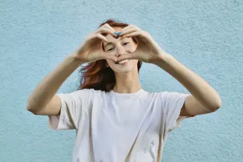Organspenden retten Leben: Junge Frau bildet mit beiden Händen ein Herz und lächelt in die Kamera.