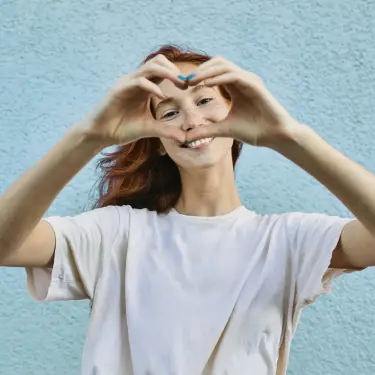 Organspenden retten Leben: Junge Frau bildet mit beiden Händen ein Herz und lächelt in die Kamera.