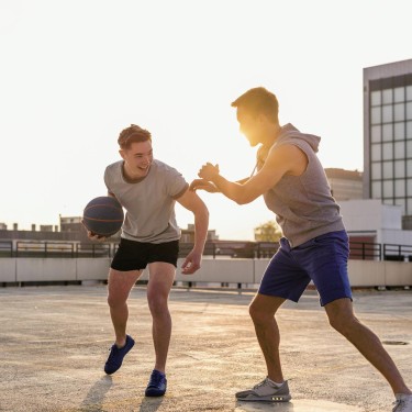 Sport ist wichtig für die Gesundheit: Zwei junge Männer spielen Basketball auf einem Parkhausdach.