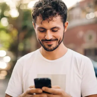 Mann schaut auf Smartphone, das er mit beiden Händen hält.
