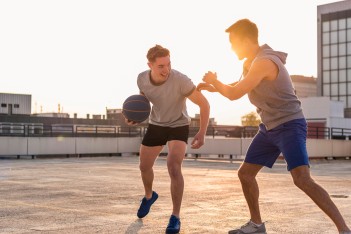 Zwei junge Männer spielen Basketball bei Sonnenuntergang auf einer Dachterrasse