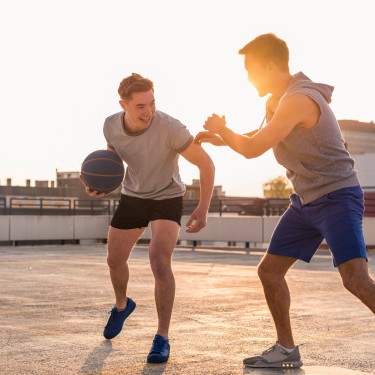 Zwei junge Männer spielen Basketball bei Sonnenuntergang auf einer Dachterrasse