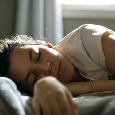 Junge Frau liegt schlafend auf einem Bett