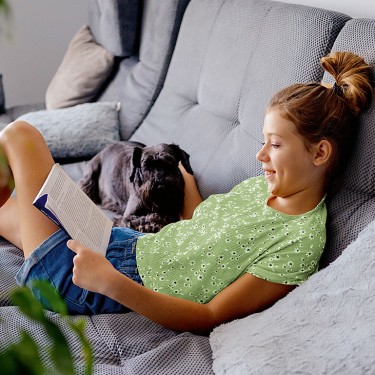 Junge Frau sitzt mit einem Hund und einem Buch auf dem Sofa