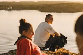 Drei junge Menschen sitzen bei Sonnenuntergang am Wasser