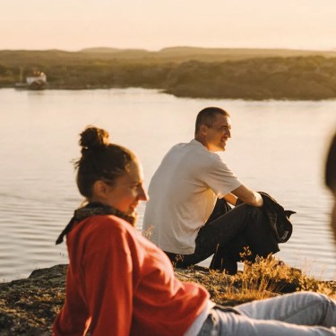 Drei junge Menschen sitzen bei Sonnenuntergang am Wasser