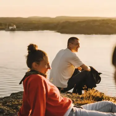 Drei junge Menschen sitzen bei Sonnenuntergang am Wasser