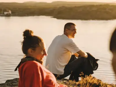 Drei junge Menschen sitzen bei Sonnenuntergang am Wasser