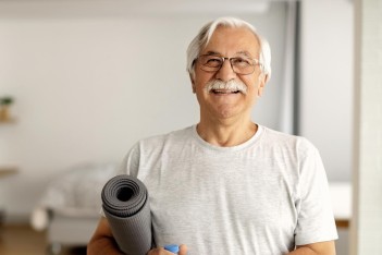 Älterer Mann im Sportoutfit hält eine eingerollte Sportmatte unter dem Arm