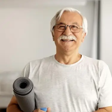 Älterer Mann im Sportoutfit hält eine eingerollte Sportmatte unter dem Arm