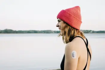 Frau steht mit Badeanzug und Mütze am Ufer