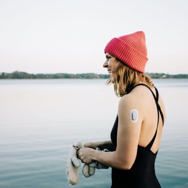 Frau steht mit Badeanzug und Mütze am Ufer