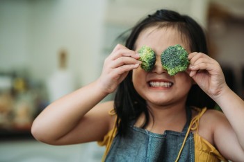 Weniger Zucker: Mädchen hält 2 Brokkoliröschen vors Gesicht