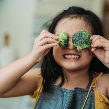 Weniger Zucker: Mädchen hält 2 Brokkoliröschen vors Gesicht