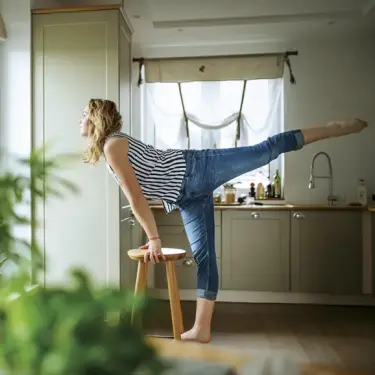 Frau im offenen Wohnbereich macht spontan Yoga auf einem Hocker