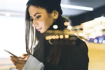 Frau abends an einem öffentlichen Ort - hinter einer Scheibe - schaut auf ihr Handy