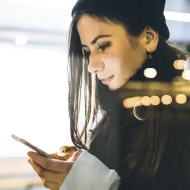 Frau abends an einem öffentlichen Ort - hinter einer Scheibe - schaut auf ihr Handy