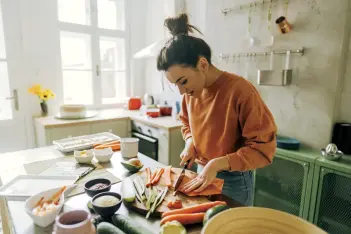 Frau schneidet auf einem Schneidebrett in der Küche Karotten und anderes Gemüse