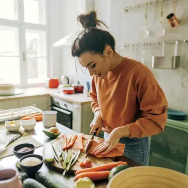 Frau schneidet auf einem Schneidebrett in der Küche Karotten und anderes Gemüse