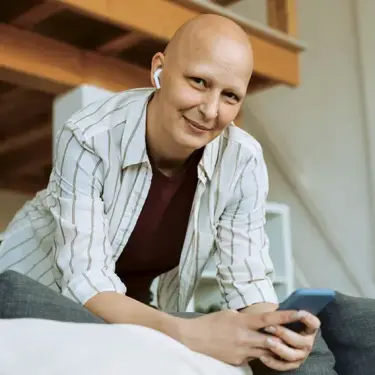 Frau lehnt sich nach vorne und lächelt in die Kamera, mit Smartphone in der Hand