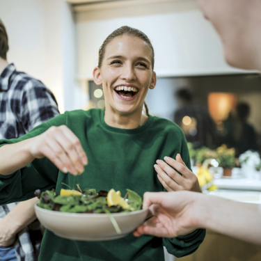 Frau in grünem Sweatshirt verfeinert freudestrahlend ihr Essen