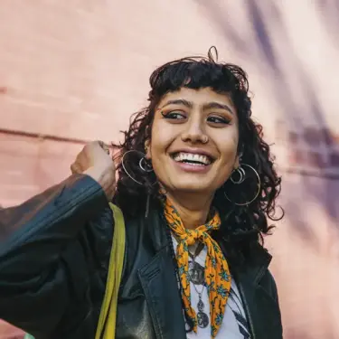 Gut gekleidete Frau mit Locken schaut lächelnd in die Kamera