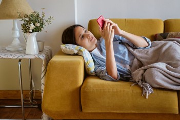 Kranke Frau liegt mit dem Smartphone zu Hause auf der Couch