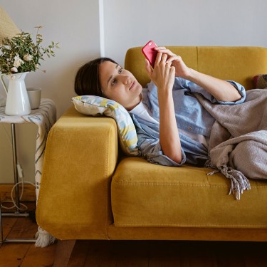 Kranke Frau liegt mit dem Smartphone zu Hause auf der Couch