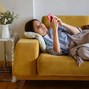 Kranke Frau liegt mit dem Smartphone zu Hause auf der Couch