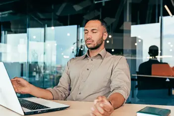 Mann meditiert mit geschlossenen Augen vor seinem Laptop