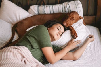 Junge Frau liegt mit einem Hund schlafend in einem Bett