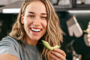 Frau isst eine Avocado in einer Küche