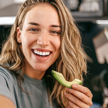 Frau isst eine Avocado in einer Küche